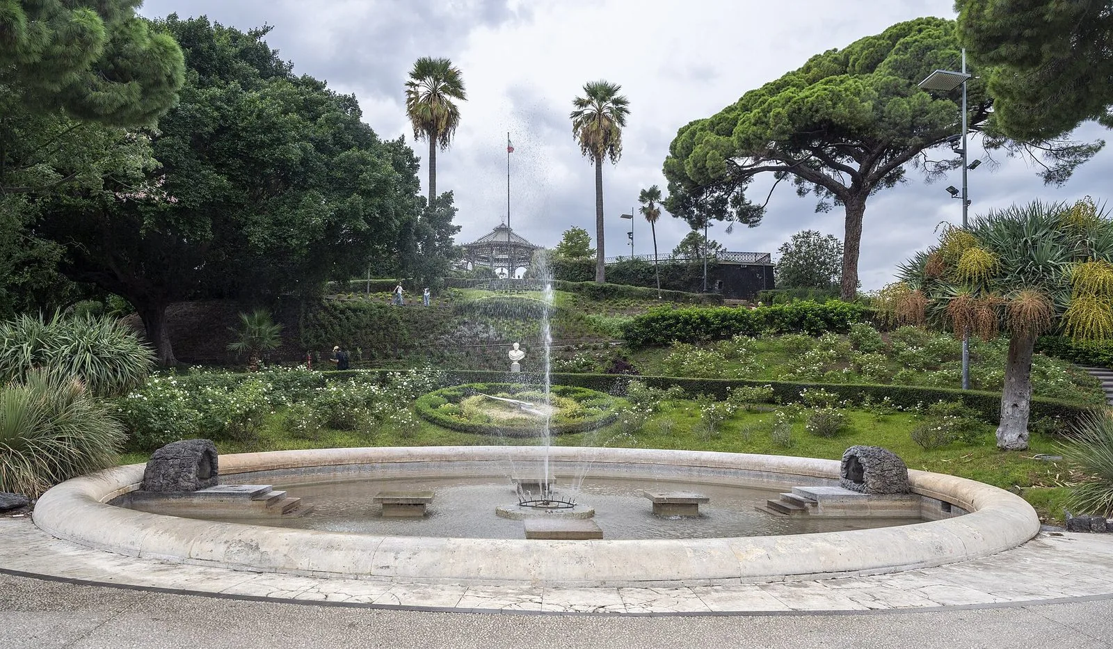 La fontana all'ingresso principale della Villa Bellini a Catania, con aiuole fiorite, palme e pini sullo sfondo