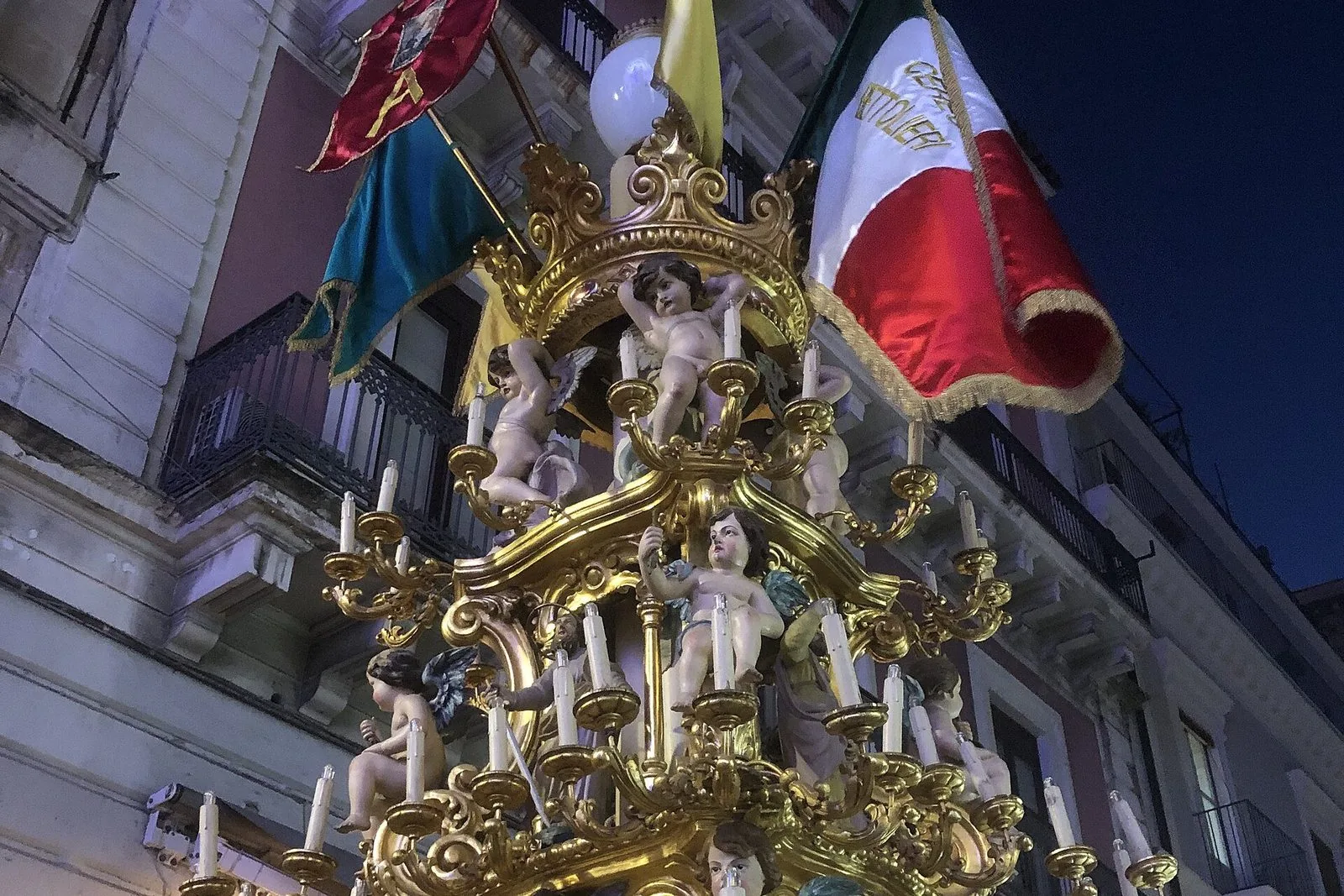 Particolare di una candelora dorata con angeli scolpiti, candele e stendardi, di sera tra i palazzi del centro di Catania durante la festa di Sant'Agata